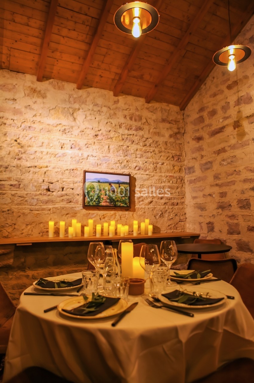 Table dressée avec élégance dans une salle en pierre, éclairée par des bougies et des suspensions lumineuses.