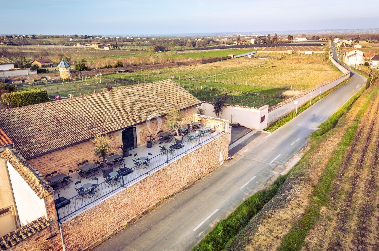 Vue aérienne d'une terrasse aménagée sur un bâtiment en briques, entourée de champs et d'une route de campagne.