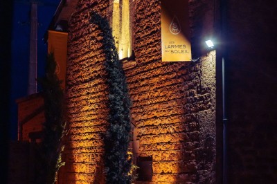 Façade en pierre éclairée d'une bâtisse ancienne avec une enseigne lumineuse, vue de nuit.