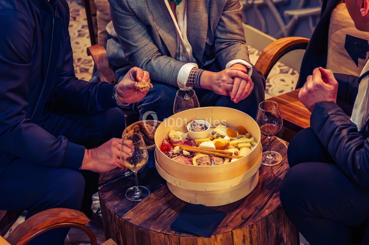 Trois personnes partagent un plateau de fromages et charcuteries autour d'une table en bois avec des verres de vin.