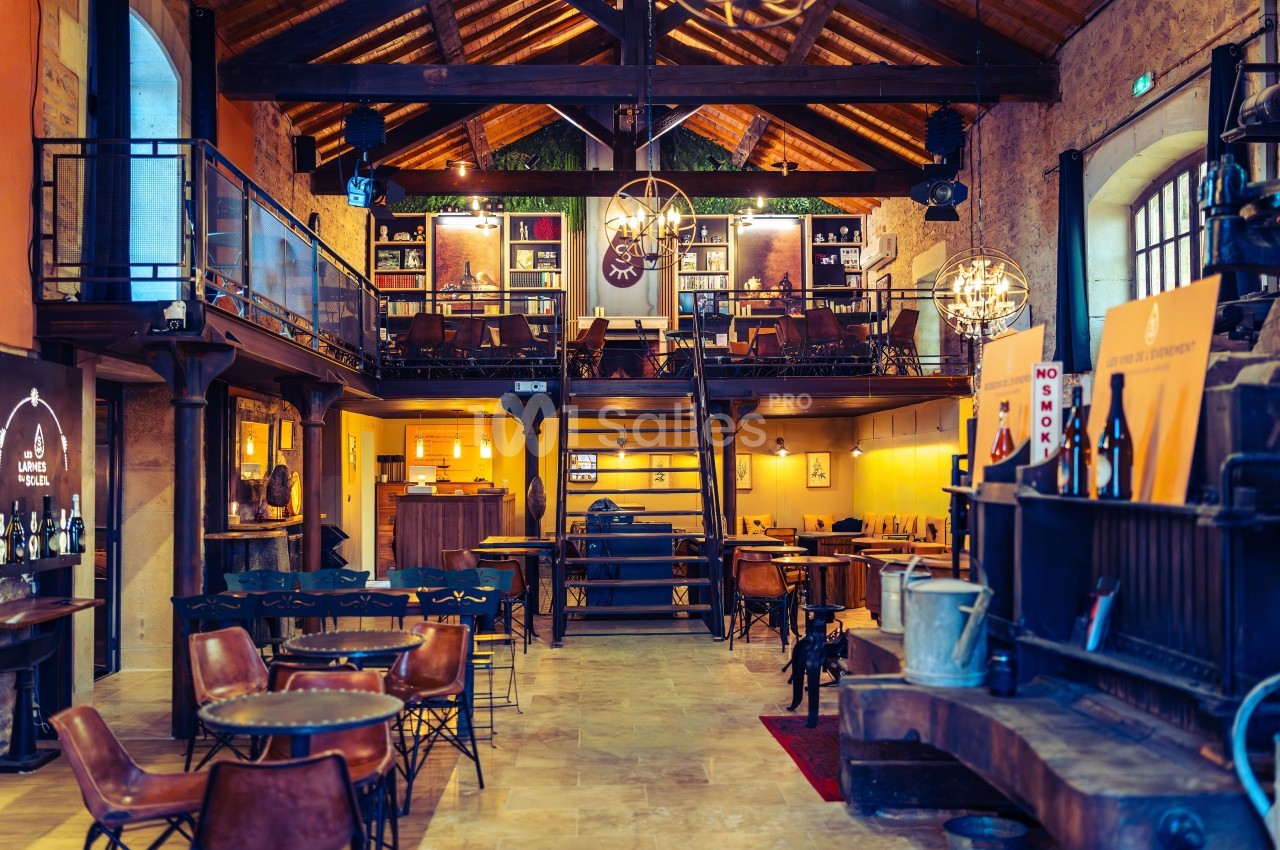 Intérieur d'un bar ou restaurant avec mezzanine, tables en bois, éclairage chaleureux et décor rustique.