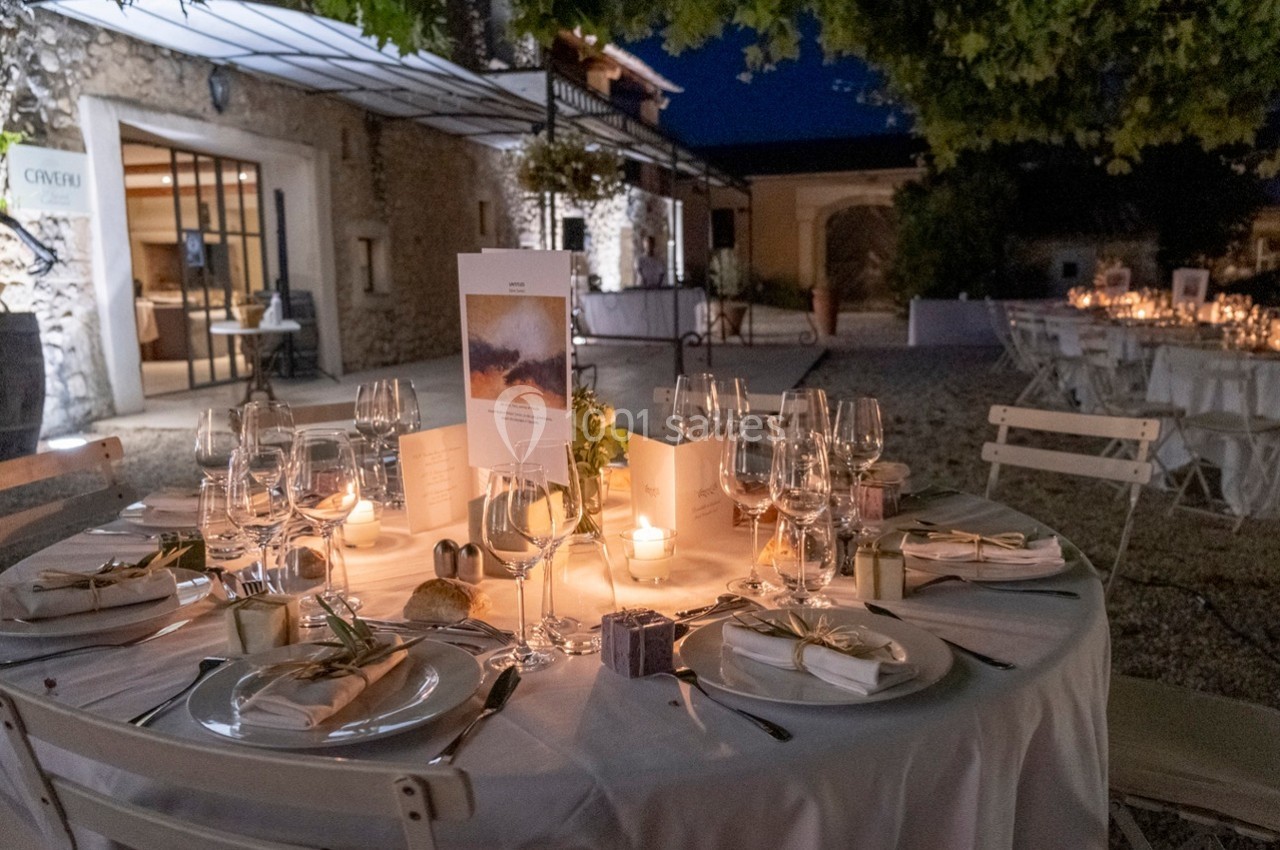 Table élégamment dressée en extérieur, éclairée par des bougies, avec vaisselle raffinée et décorations soignées.
