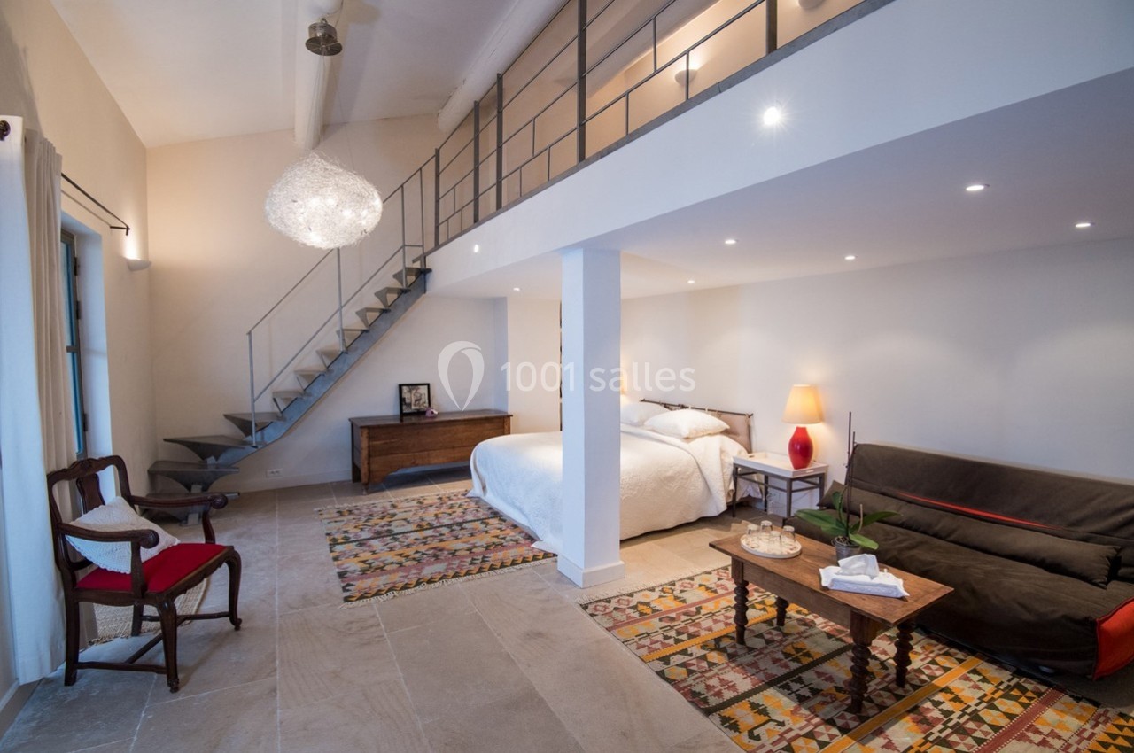 Chambre lumineuse avec lit double, canapé, tapis colorés, escalier métallique et décoration moderne.