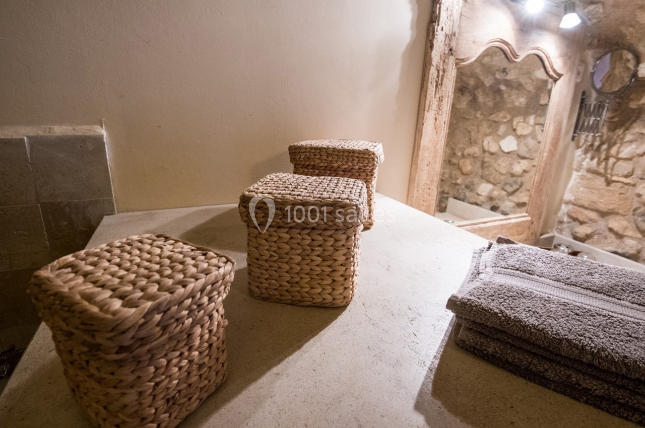 Trois paniers en osier et des serviettes pliées posés sur un plan de travail en pierre dans une salle de bain rustique.