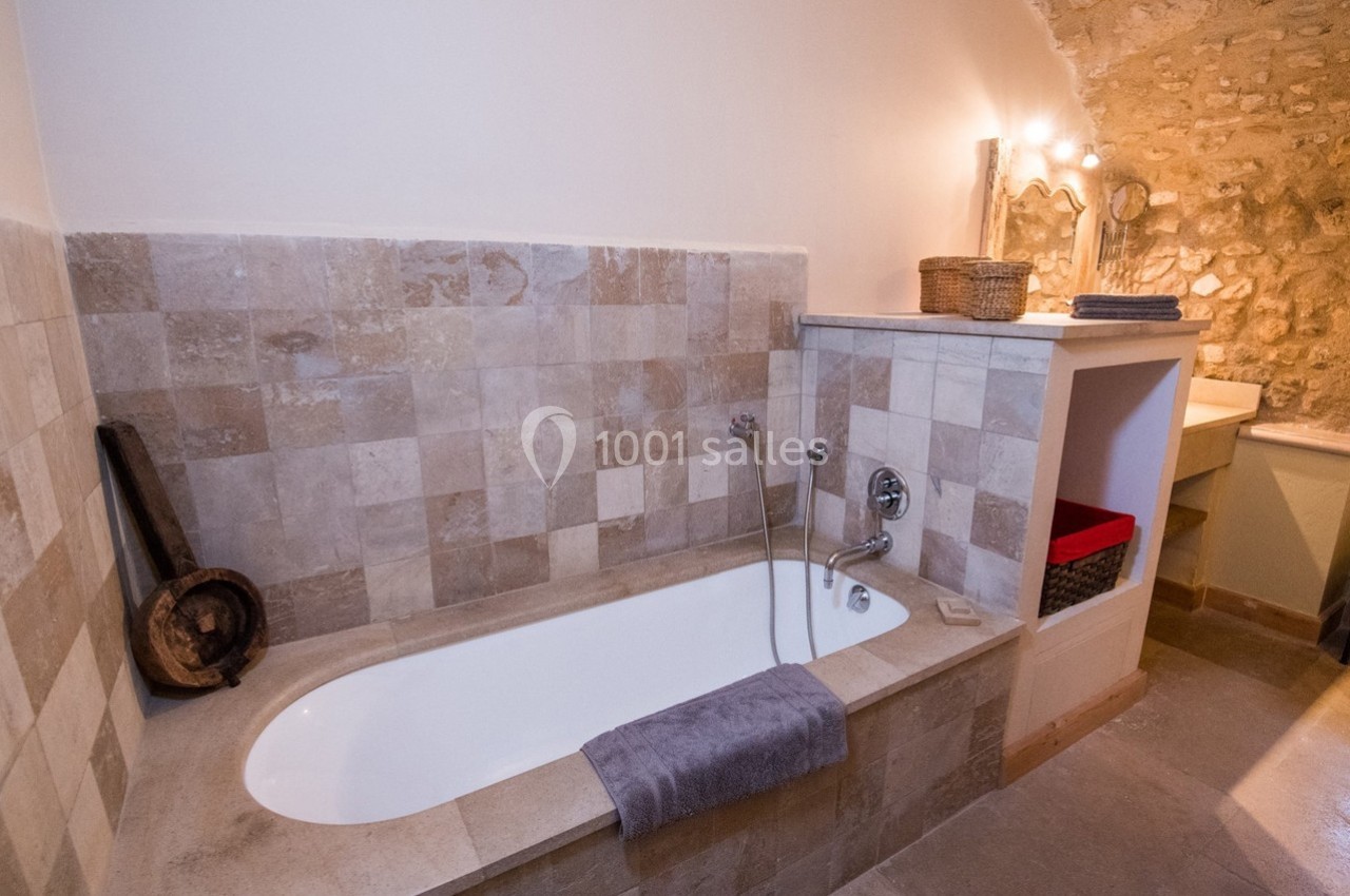 Salle de bain avec baignoire encastrée en pierre, murs carrelés, éclairage doux et éléments décoratifs rustiques.