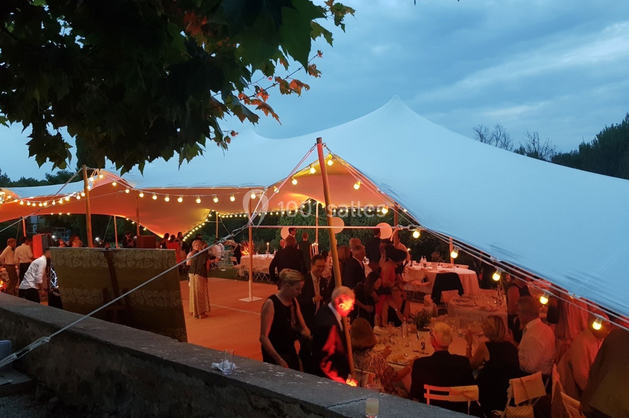 Tente blanche éclairée par des guirlandes lumineuses, abritant des convives lors d'un événement en soirée.