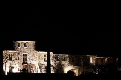 Façade d'un bâtiment en pierre éclairée la nuit, entourée de végétation sombre.