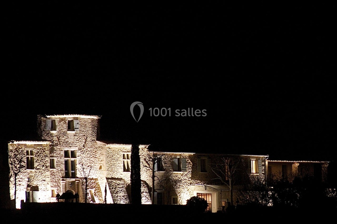 Façade d'un bâtiment en pierre éclairée la nuit, entourée de végétation sombre.