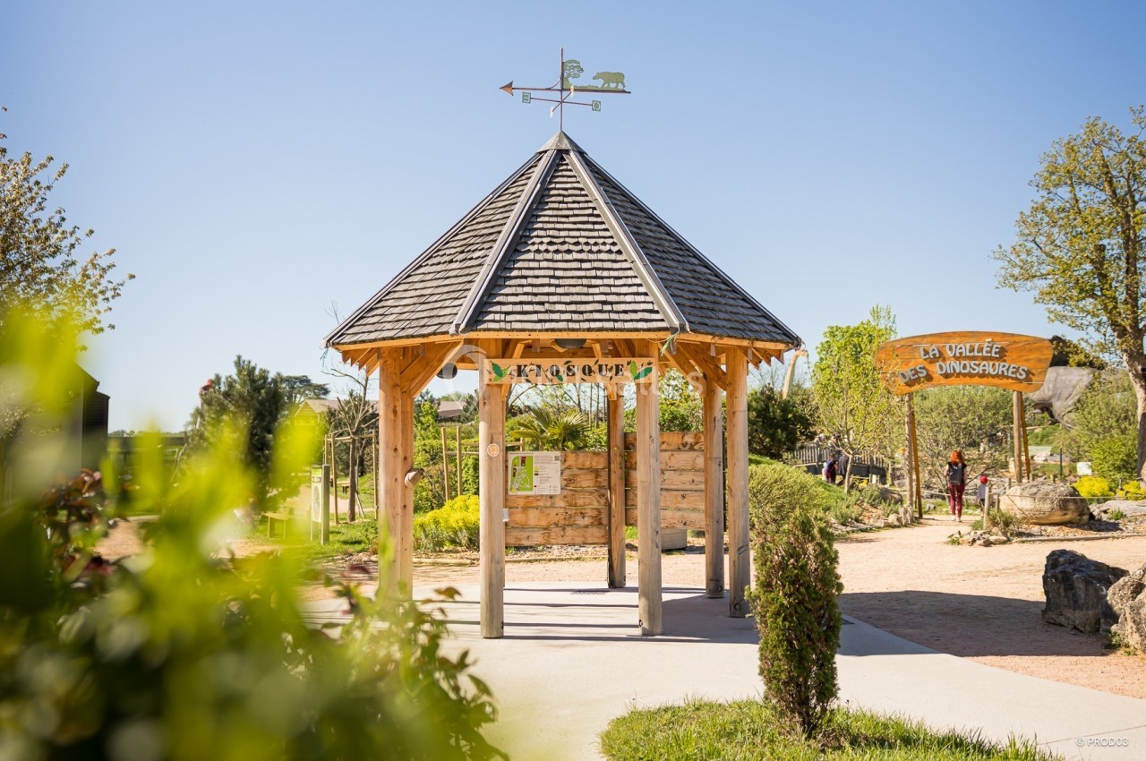 Kiosque en bois avec une girouette, entouré de verdure, près d'une entrée indiquant ’La Vallée des Dinosaures’.