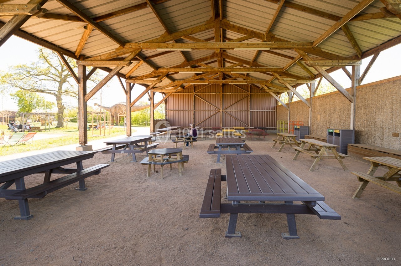 Abri en bois ouvert avec tables de pique-nique, situé dans un espace extérieur ensoleillé.