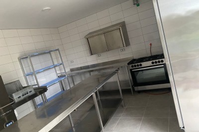 Cuisine professionnelle avec équipements en acier inoxydable, comprenant un four, des étagères et des plans de travail.