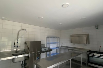 Cuisine professionnelle avec équipements en acier inoxydable, comprenant un four, des étagères et des plans de travail.