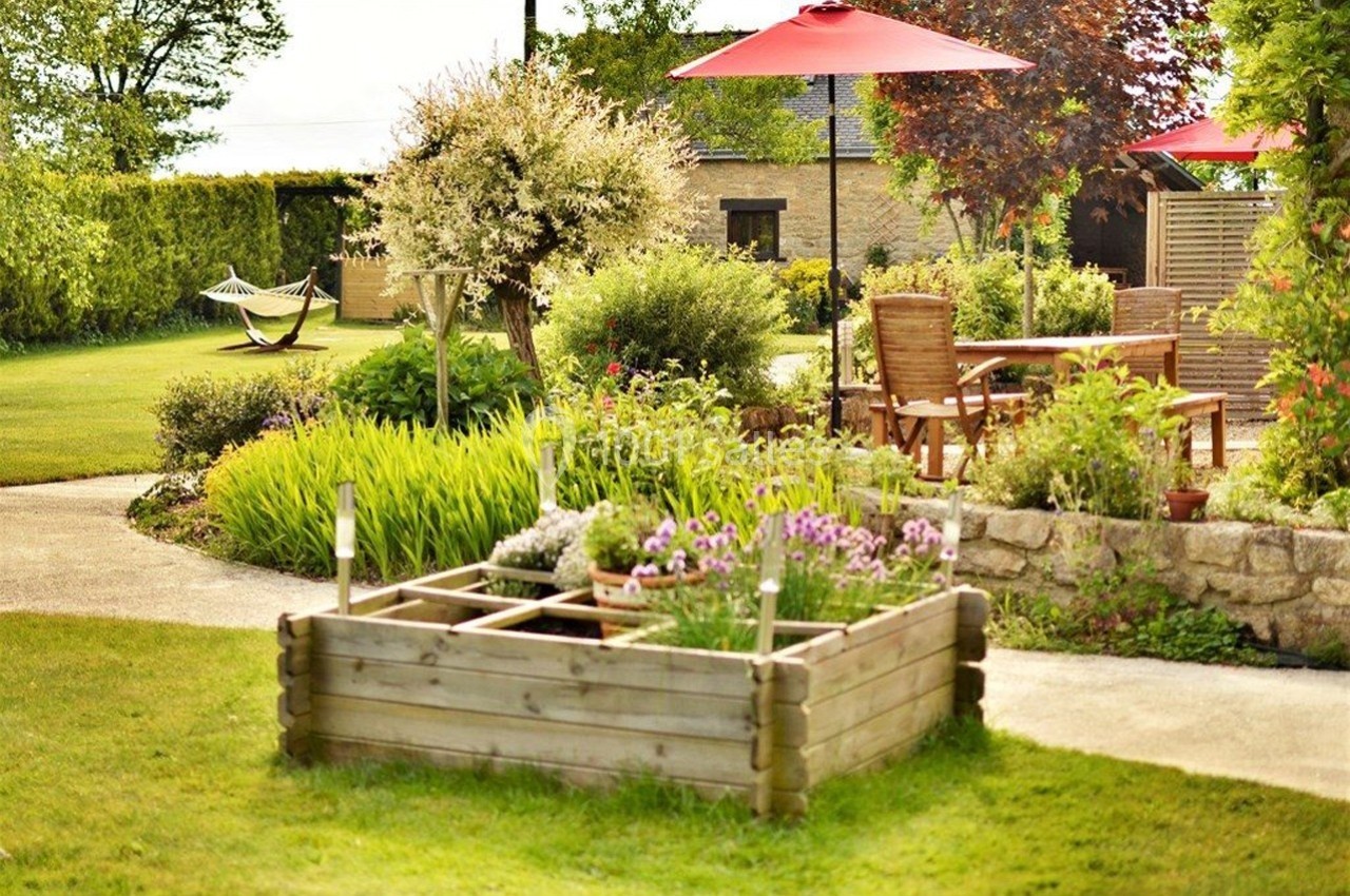 Jardin aménagé avec parterre surélevé, mobilier de jardin sous parasols rouges et hamac en arrière-plan.