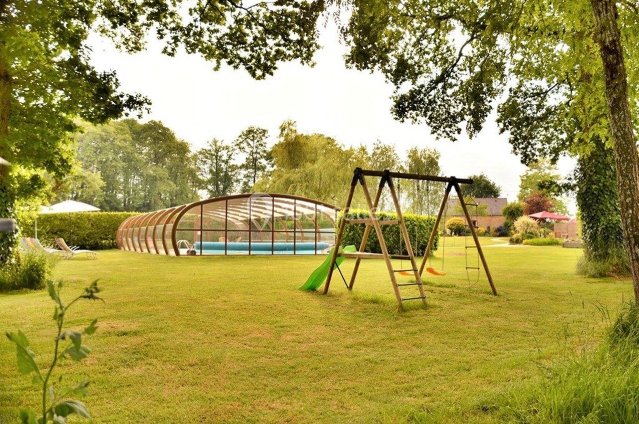 Jardin avec balançoire, pelouse bien entretenue et piscine couverte entourée de verdure.