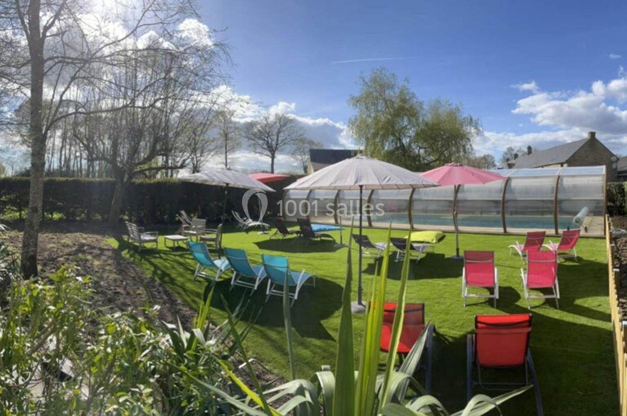 Chaises longues colorées et parasols disposés autour d'une piscine couverte dans un jardin ensoleillé.