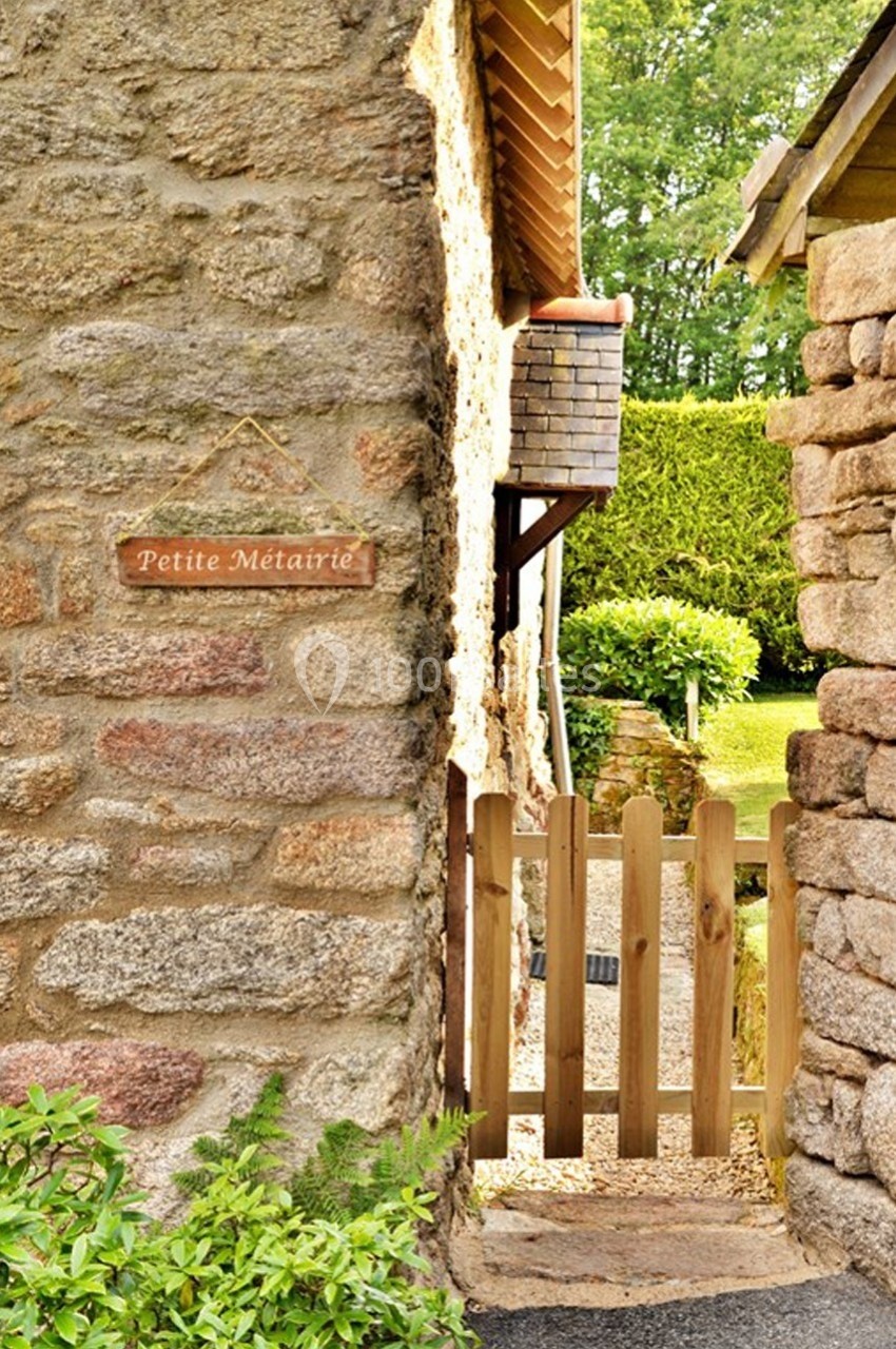Mur en pierre avec une pancarte ’Petite Métairie’, une barrière en bois et un jardin verdoyant en arrière-plan.