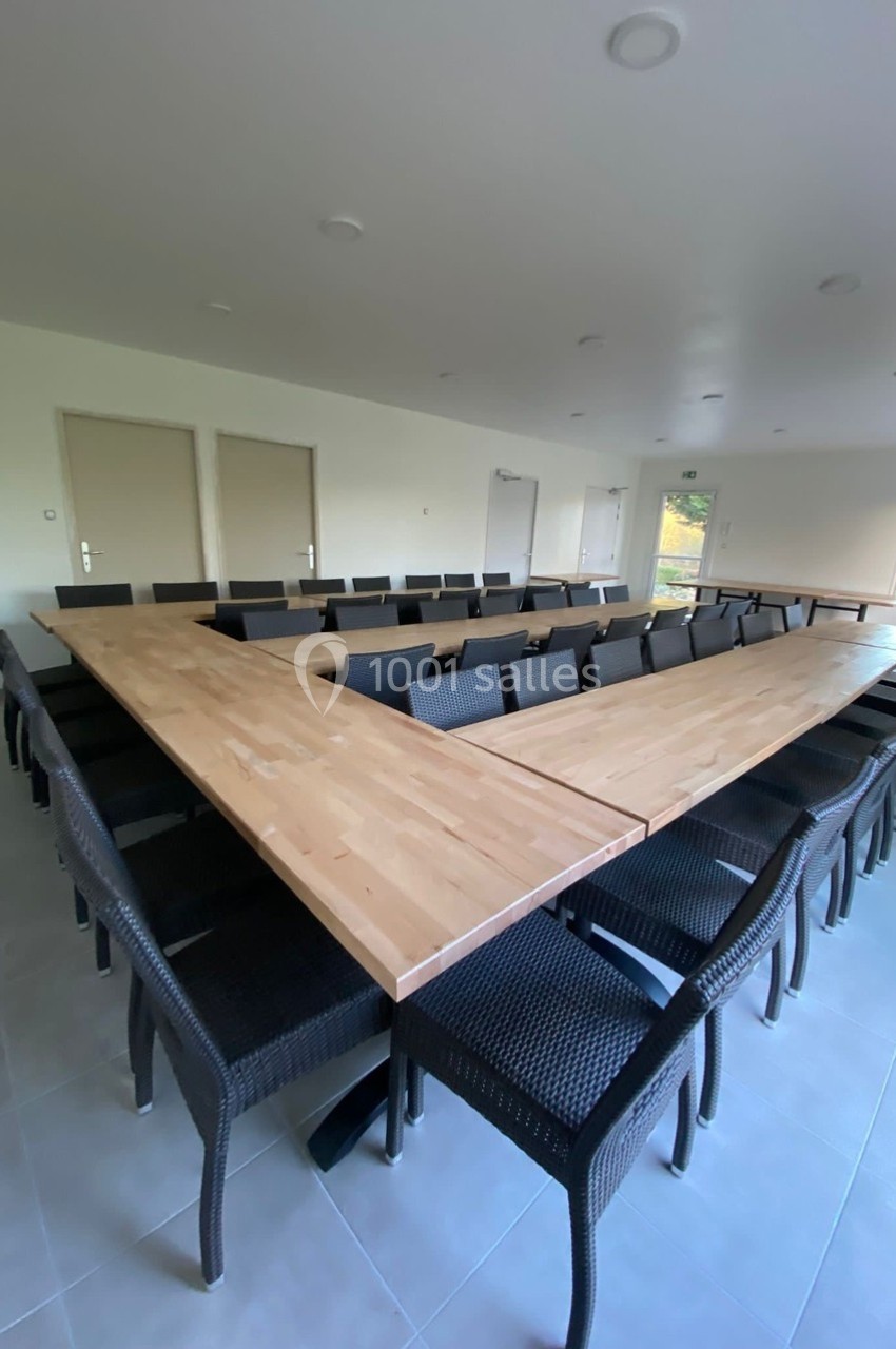 Salle de réunion avec une grande table en forme de U entourée de chaises noires, éclairée par la lumière naturelle.