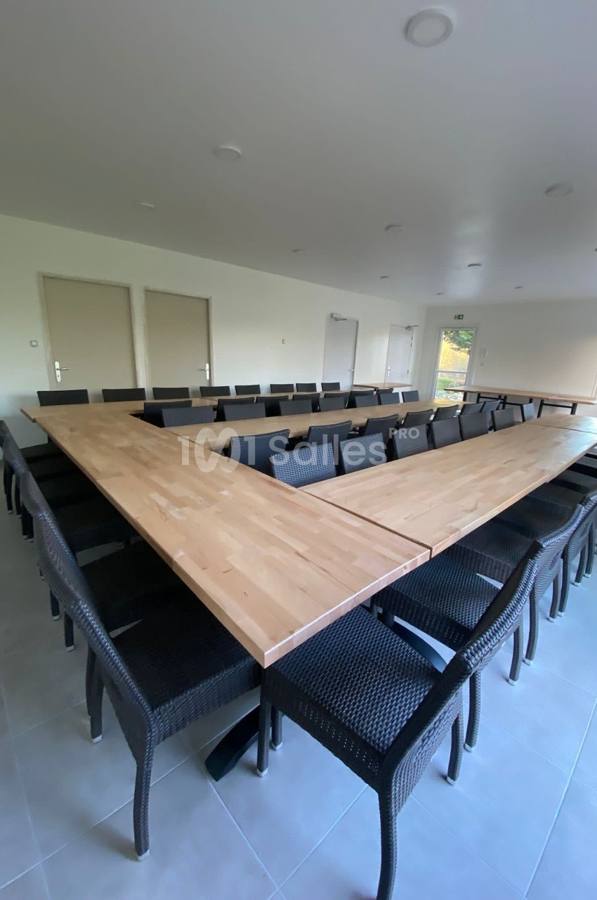 Salle de réunion avec une grande table en forme de U entourée de chaises noires, éclairée par la lumière naturelle.