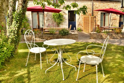 Jardin verdoyant avec pelouse, arbres dénudés, fleurs printanières et ciel bleu parsemé de nuages légers.
