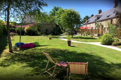 Jardin verdoyant avec pelouse, arbres dénudés, fleurs printanières et ciel bleu parsemé de nuages légers.