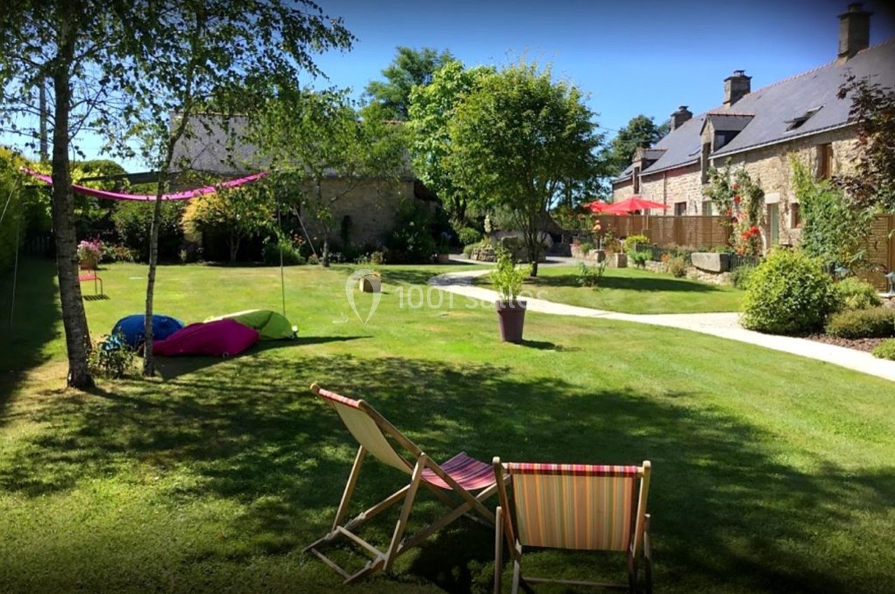 Jardin verdoyant avec chaises longues, arbres, pelouse bien entretenue et bâtiments en pierre en arrière-plan.