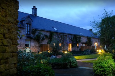 Jardin verdoyant avec pelouse, arbres dénudés, fleurs printanières et ciel bleu parsemé de nuages légers.