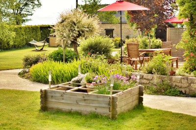 Jardin verdoyant avec pelouse, arbres dénudés, fleurs printanières et ciel bleu parsemé de nuages légers.