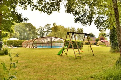 Jardin verdoyant avec pelouse, arbres dénudés, fleurs printanières et ciel bleu parsemé de nuages légers.