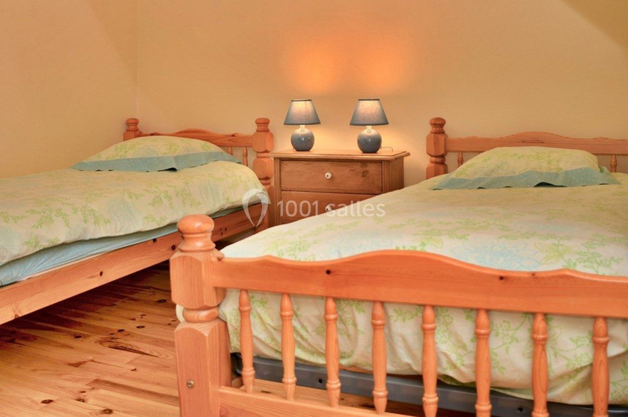 Deux lits simples en bois avec une table de chevet et deux lampes allumées dans une chambre aux tons chaleureux.