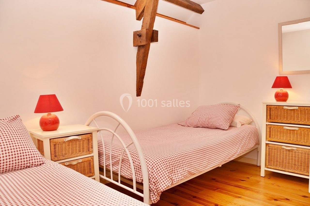 Deux lits simples avec linge à carreaux rouges, deux lampes assorties et des meubles en osier dans une chambre lumineuse.