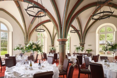 Salon spacieux avec poutres apparentes, mobilier classique, canapés rouges, fauteuils rayés et lumière naturelle.