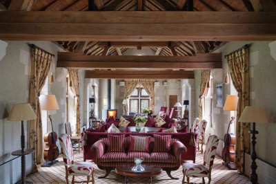 Salon spacieux avec poutres apparentes, mobilier classique, canapés rouges, fauteuils rayés et lumière naturelle.