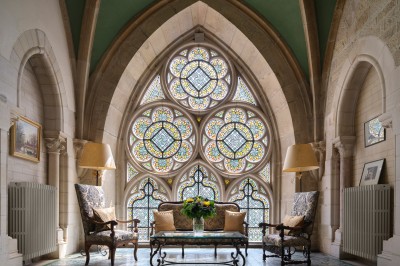 Chambre élégante avec un lit double, papier peint floral, fenêtres à vitraux et mobilier classique en bois.