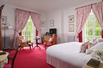 Chambre élégante avec un lit double, papier peint floral, fenêtres à vitraux et mobilier classique en bois.