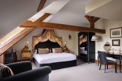 Chambre élégante avec un lit double, papier peint floral, fenêtres à vitraux et mobilier classique en bois.