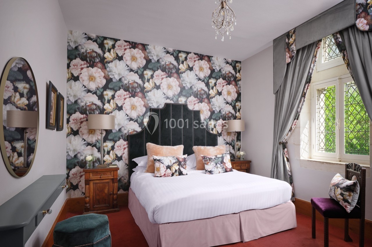 Chambre élégante avec un lit double, papier peint floral, fenêtres à vitraux et mobilier classique en bois.