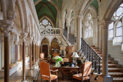 Chambre élégante avec un lit double, papier peint floral, fenêtres à vitraux et mobilier classique en bois.