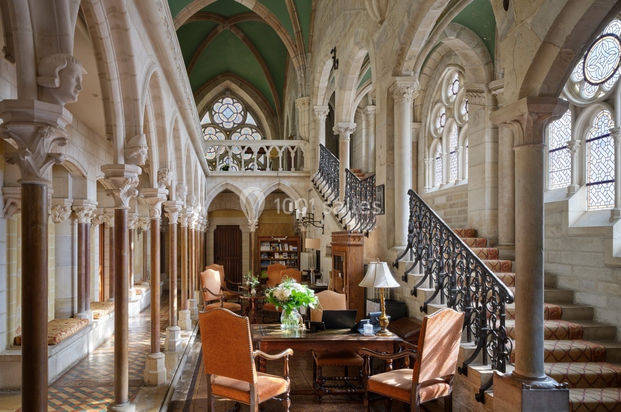 Intérieur lumineux d'un bâtiment historique avec colonnes, arches, escalier en fer forgé et mobilier classique.