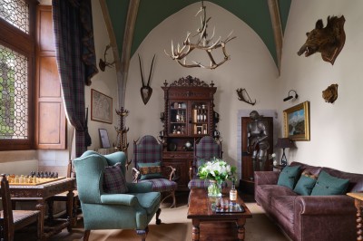 Chambre élégante avec un lit double, papier peint floral, fenêtres à vitraux et mobilier classique en bois.