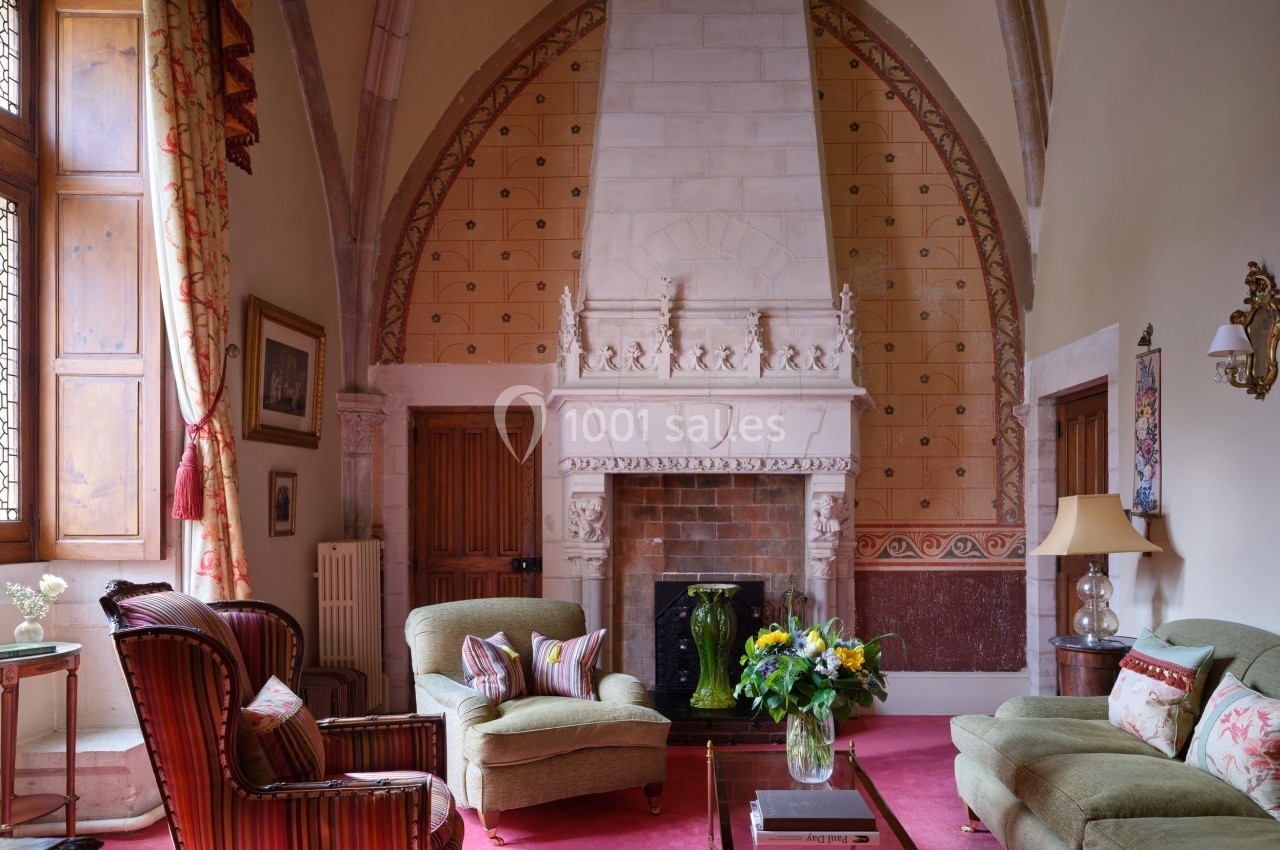Salon avec cheminée en pierre sculptée, fauteuils, canapé, table basse avec fleurs et décorations classiques.