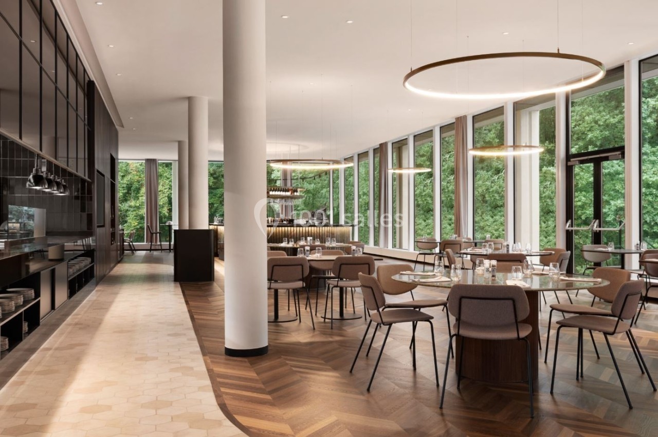 Salle de restaurant moderne avec grandes baies vitrées, mobilier élégant et vue sur un espace arboré.
