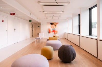 Femme assise dans un hammam aux carreaux roses, enveloppée dans une serviette blanche.
