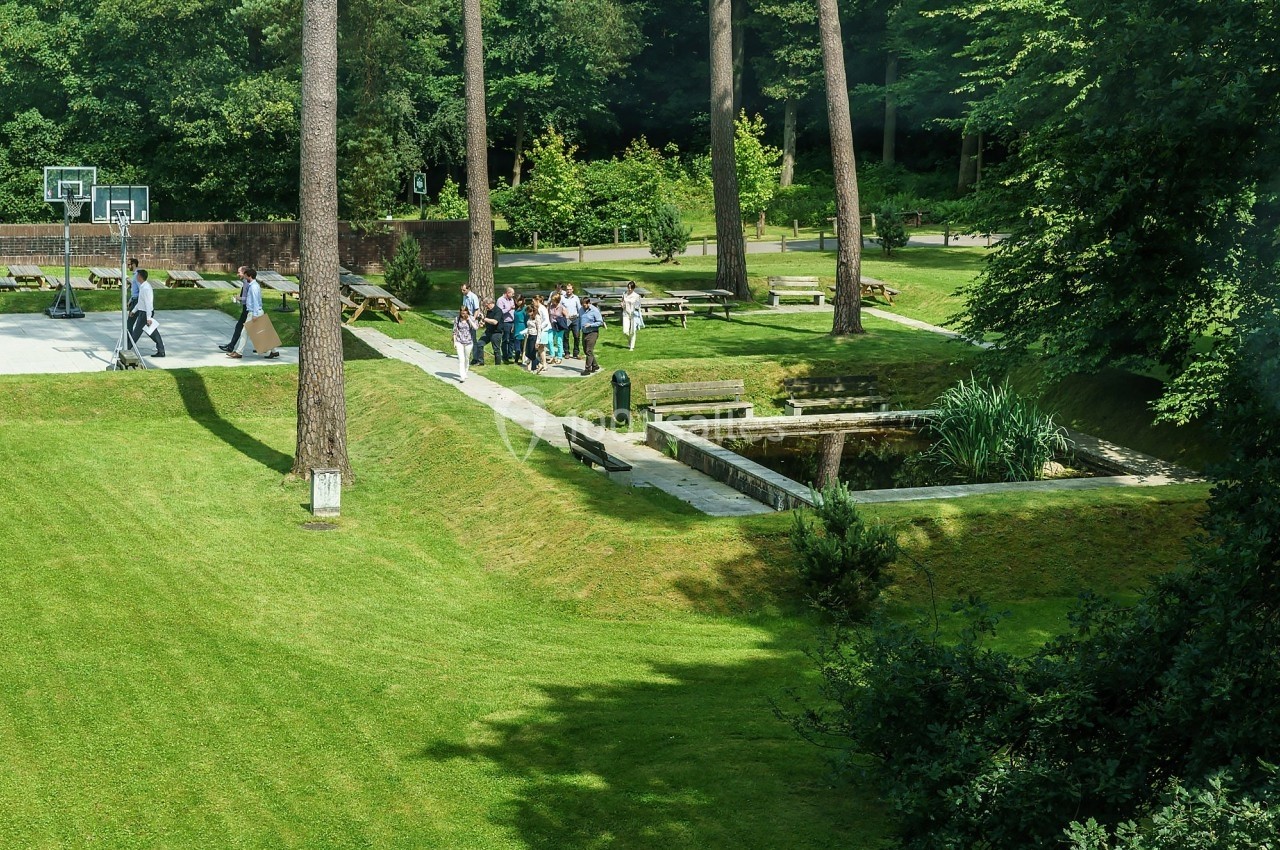 Un groupe de personnes rassemblées près d'un étang dans un parc verdoyant avec un terrain de basket à proximité.
