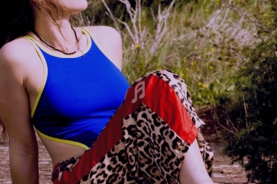 Femme assise dehors, portant un haut bleu, un pantalon à motif léopard et des lunettes originales en forme de fleurs.