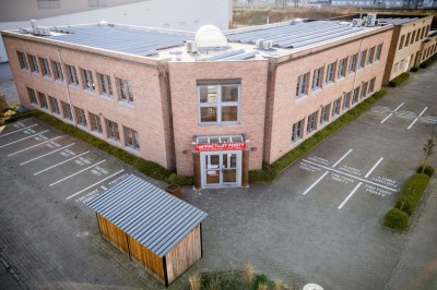 Bâtiment en briques à deux étages avec un parking adjacent et un abri en bois au premier plan.