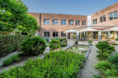 Bâtiment en briques à deux étages avec un parking adjacent et un abri en bois au premier plan.