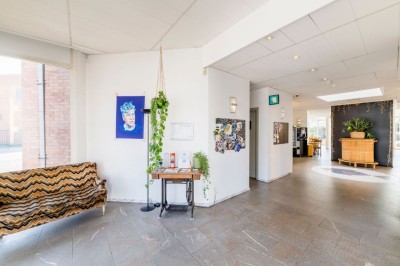 Bâtiment en briques à deux étages avec un parking adjacent et un abri en bois au premier plan.