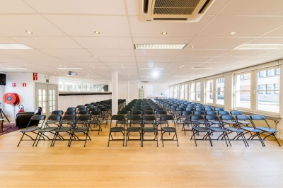 Bâtiment en briques à deux étages avec un parking adjacent et un abri en bois au premier plan.