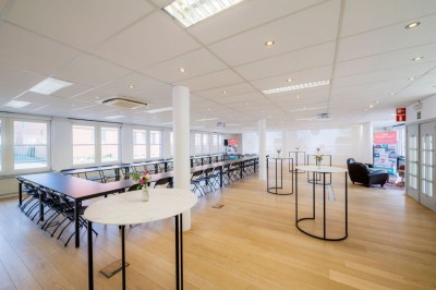 Bâtiment en briques à deux étages avec un parking adjacent et un abri en bois au premier plan.