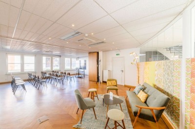 Bâtiment en briques à deux étages avec un parking adjacent et un abri en bois au premier plan.